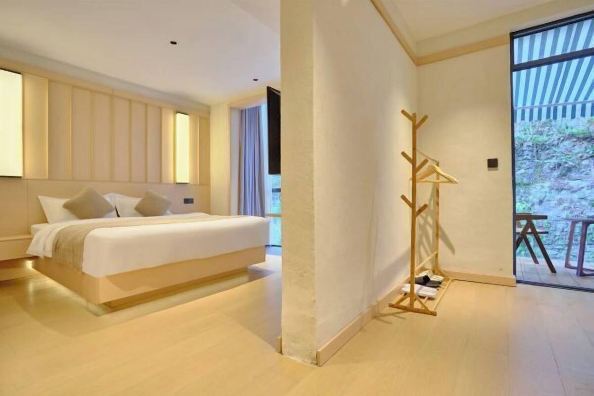 A modern bedroom with a large bed, a wooden floor, and a view of the outdoors through a large window.