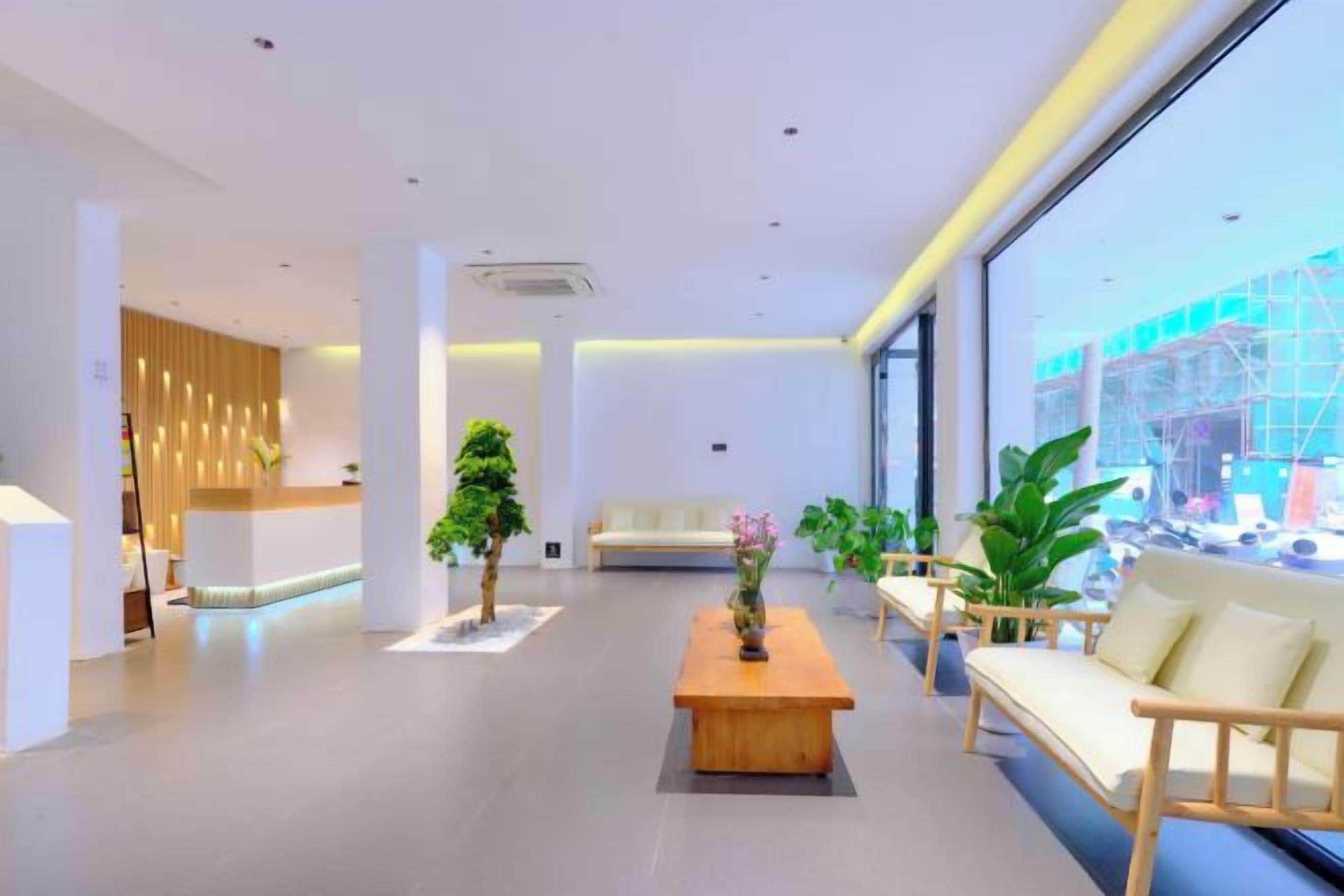 A modern hotel lobby with a reception desk, seating area, and large windows offering a view of the outside.