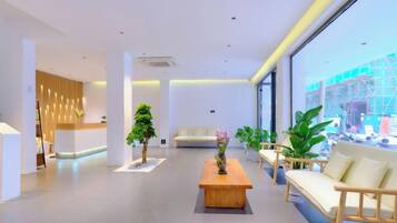 A modern hotel lobby with a reception desk, seating area, and large windows offering a view of the outside.
