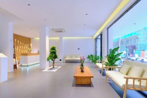A modern hotel lobby with a reception desk, seating area, and large windows offering a view of the outside. - Yishan Xiaozhu (Yangshuo West Street store) (Yangshuo)