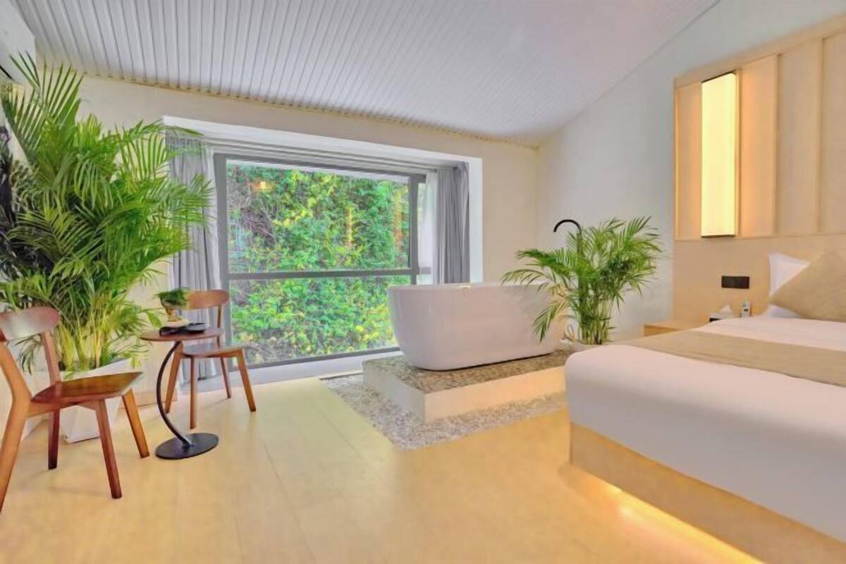 A modern bedroom with a large window, a bathtub, and several potted plants.