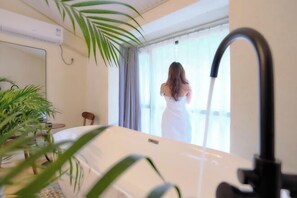 A room with a bathtub, a window with curtains, and a potted plant. - Yishan Xiaozhu (Yangshuo West Street store) (Yangshuo)