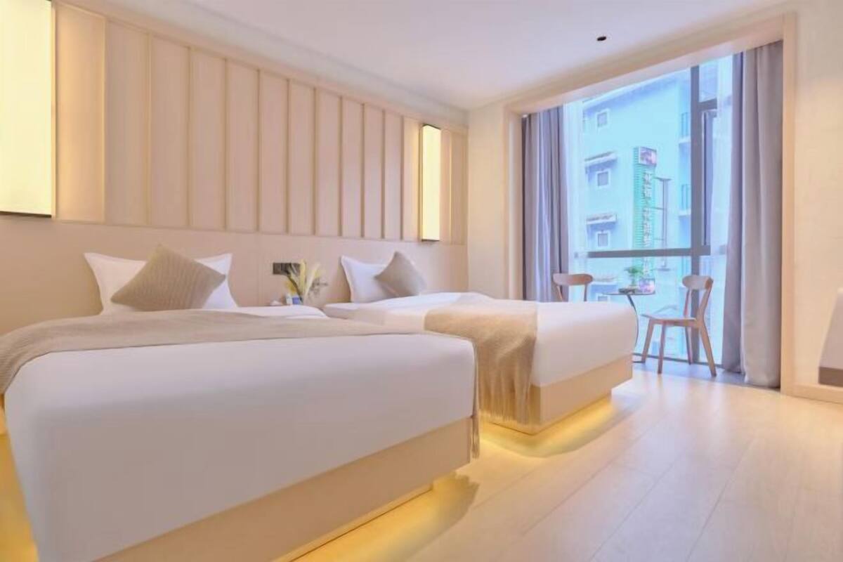 A hotel room with two beds, a large window with a view, and a small table with a chair.