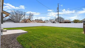 Un jardin avec une clôture blanche, une pelouse verdoyante et une terrasse en béton.