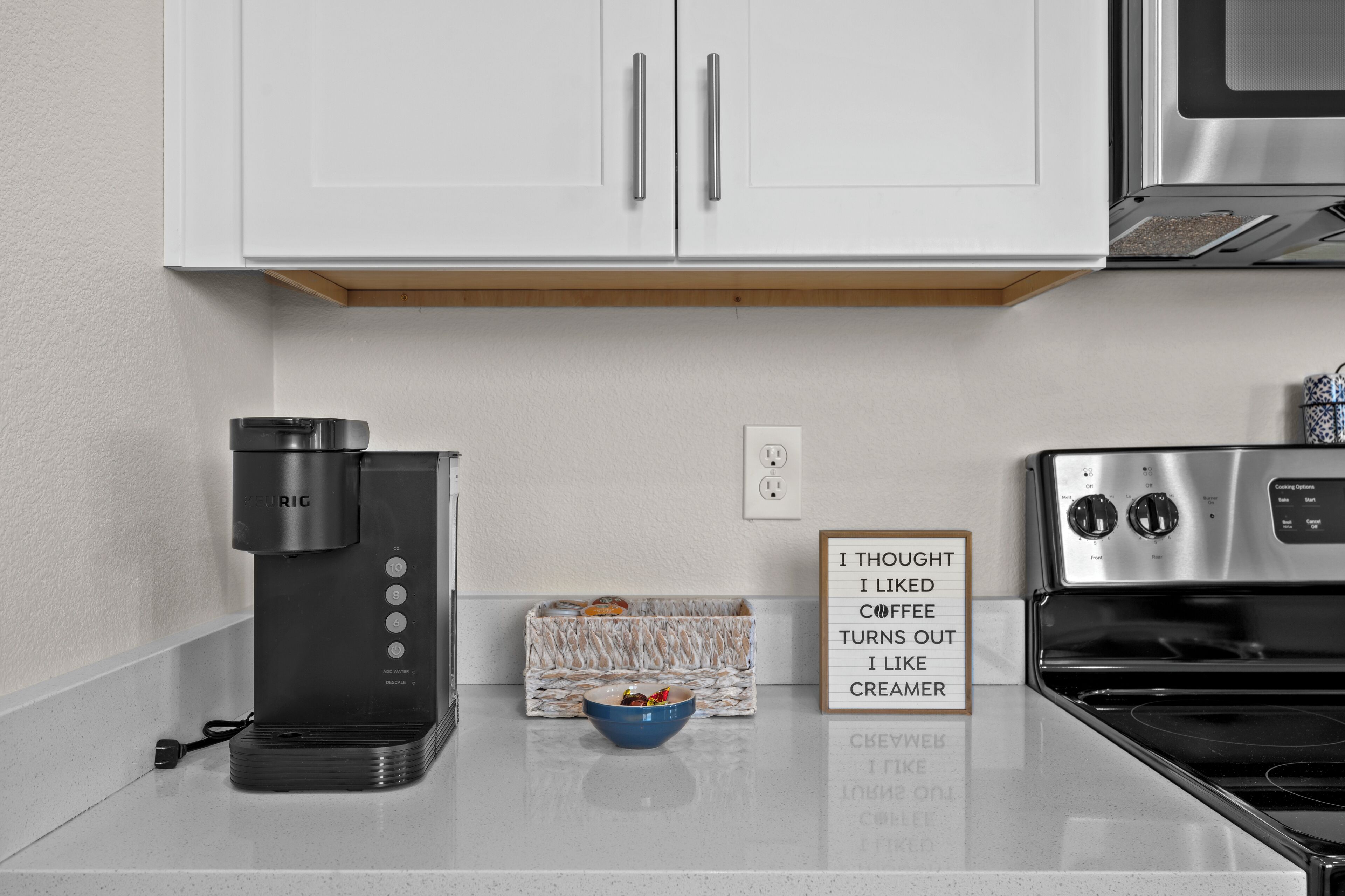 Una cucina con mobili bianchi, una macchina da caffè, una ciotola e un cartello.