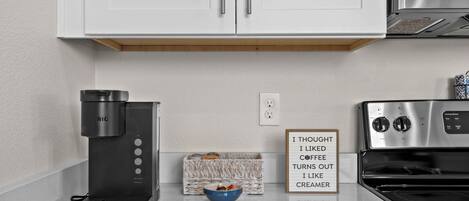 Una cucina con mobili bianchi, una macchina da caffè, una ciotola e un cartello.