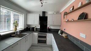 Una cocina moderna con armarios blancos, una estufa negra y una pared de acento rosa.