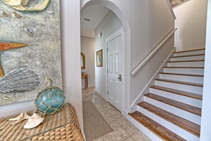 A staircase with wooden steps and white walls, leading to a room with a door and a framed picture on the wall. - "Seas The Day!" Luxe Villa | Pool, Pickleball & Steps to Beach (Panama City Beach)