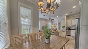 Ein Essbereich mit Holztisch, Stühlen, einer Chandelierleuchtre und Blick zur Küche.