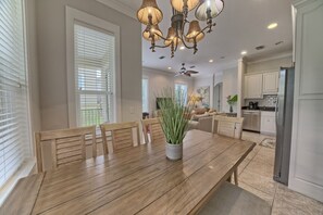 Un coin repas avec une table en bois, des chaises, un lustre et une vue sur la cuisine.