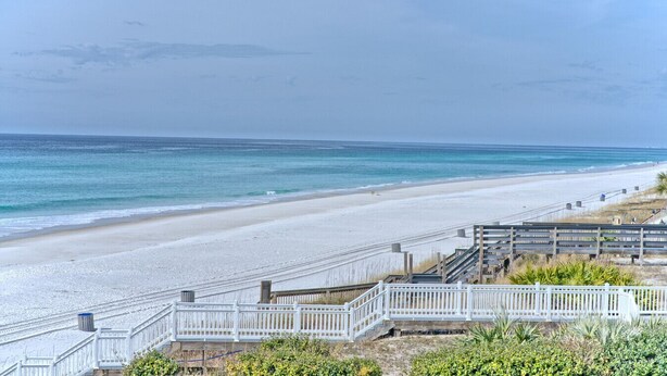 Ein Strand mit weißem Zaun, Holzstegen und freiem Blick auf den Ozean.