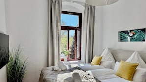 A hotel room with a large bed, a potted plant, a window with curtains, and a painting on the wall. - ElbDreams Cozy Design Apartment (Dresden)
