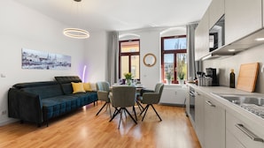 A modern living room with a sofa, chairs, a dining table, and a kitchen area with appliances. - ElbDreams Cozy Design Apartment (Dresden)