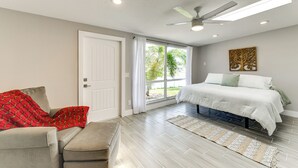 Una camera da letto con un letto, un divano, una finestra con tende e una ventola a soffitto, oltre a un elemento decorativo a parete.