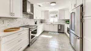 Una cucina moderna con mobili bianchi, elettrodomestici in acciaio inossidabile e una parete a mosaico in marmo.