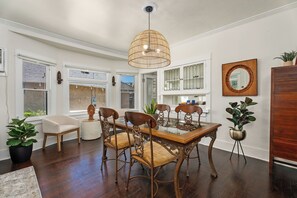 A dining area with a glass-top table, ornate chairs, a woven pendant light, and potted plants. - CozyVibeStay . King Bed. Parking. Walk to Beach (Long Beach)