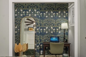 A room with a desk, chair, lamp, and a mirror reflecting a door.