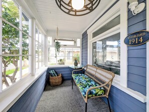 A covered porch with a wicker bench, a hanging plant, and a wall-mounted sign indicating establishment year. - CozyVibeStay . King Bed. Parking. Walk to Beach (Long Beach)