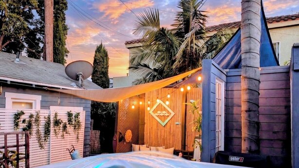 A hot tub in a backyard with a wooden fence, a satellite dish, and a decorative wall with lights. - CozyVibeStay . King Bed. Parking. Walk to Beach (Long Beach)
