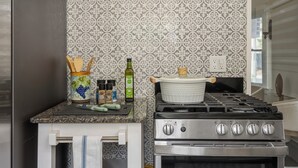 A kitchen with a patterned backsplash, a stove, and a small countertop with kitchen utensils and a pot. - CozyVibeStay . King Bed. Parking. Walk to Beach (Long Beach)