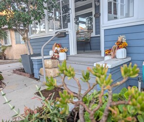 Una casa residencial con un porche adornado con flores otoñales y fardos de heno.