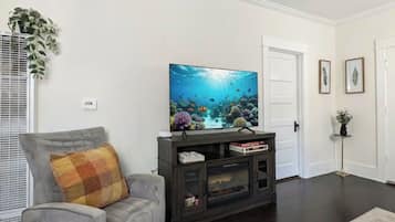 A living room with a dark wood floor, a gray sofa with a plaid cushion, a dark wood entertainment center with a flat-screen TV, and a white door.