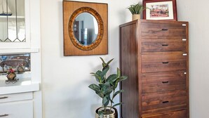 A room with a wooden cabinet, a mirror with a woven frame, a potted plant, and a framed picture on the wall. - CozyVibeStay . King Bed. Parking. Walk to Beach (Long Beach)