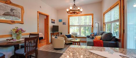A spacious living area with a large kitchen island, a dining table with chairs, a sofa, and a television.
