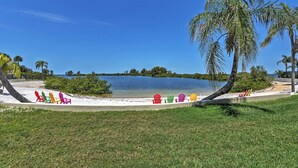 Una playa con sillas Adirondack de colores alineadas en la arena, una palmera y un lago tranquilo al fondo.