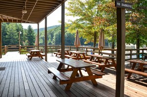 A wooden deck with picnic tables and umbrellas, overlooking a forested area. - Lake & Golf Course Views: Big Canoe Home w/ Deck! (Jasper)
