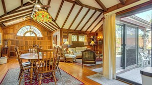 A spacious dining area with wooden furniture, a large chandelier, and a view through a glass door to the outside. - Steps to Beach: Timeless Home w/ Cotuit Bay View! (Cotuit)