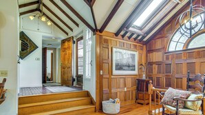 A wooden interior with a staircase, a wooden chair with cushions, and a framed picture on the wall. - Steps to Beach: Timeless Home w/ Cotuit Bay View! (Cotuit)