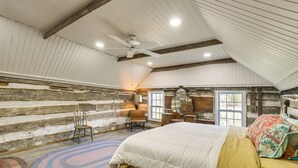 Ein Schlafzimmer mit schräg versiegelter Decke, einem Bett mit weißer und gelber Bettdecke, einem Holzstuhl, einem runden Teppich und einer Holzwand mit einem Fenster.