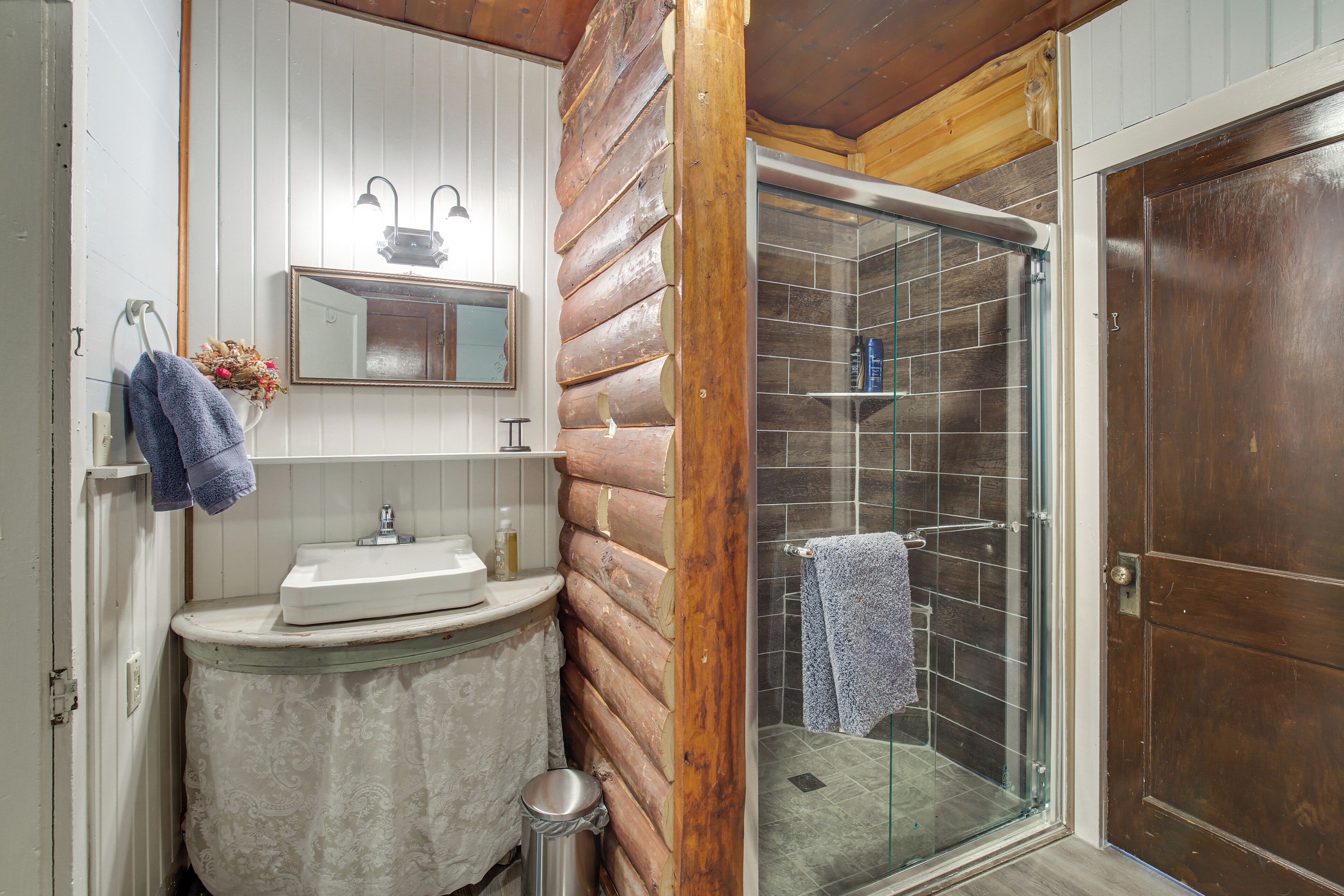 A bathroom with a wooden log wall, a sink with a mirror above it, and a glass shower enclosure.