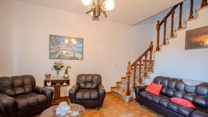 Een woonkamer met leren banken, een glazen salontafel, een schilderij van een reuzenrad en een trap met houten leuningen.