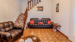 Een woonkamer met een leren bank, een leren fauteuil, een bijzettafeltje en een trap met een bakstenen muur.