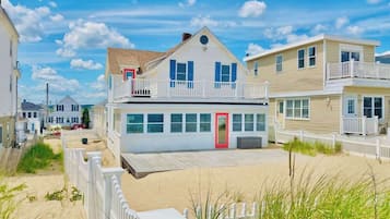 A beachfront house with a red door, white railings, and a sandy walkway.