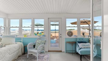 A sunlit room with a view of the beach, featuring a bed, two chairs, and a small table.