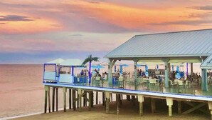 A pier with outdoor seating overlooking the sea, a covered area with tables and chairs, and a building with a metal roof.