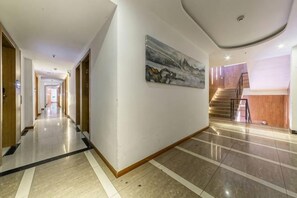 A hotel corridor with a wooden floor, a painting on the wall, and a staircase leading to another level.