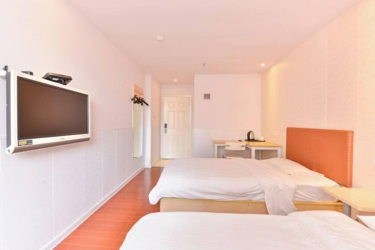 A hotel room with two beds, a TV mounted on the wall, a desk, and a door in the background.