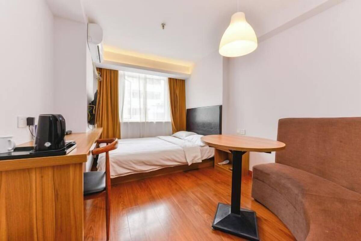 A hotel room with a bed, a small desk with a coffee maker, a round table, a sofa, and a TV.