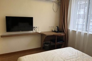 A hotel room with a bed, a desk with a chair, a television, and a window with curtains.