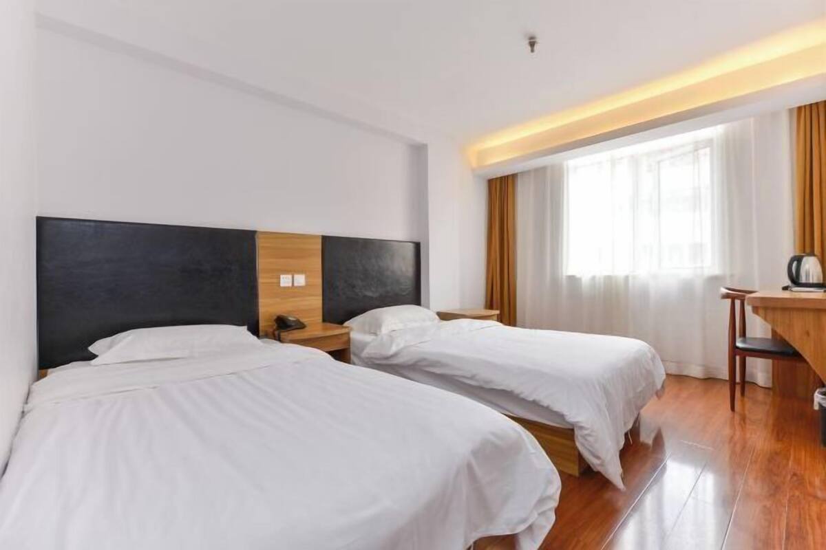 A hotel room with two beds, a desk, and a window with curtains.