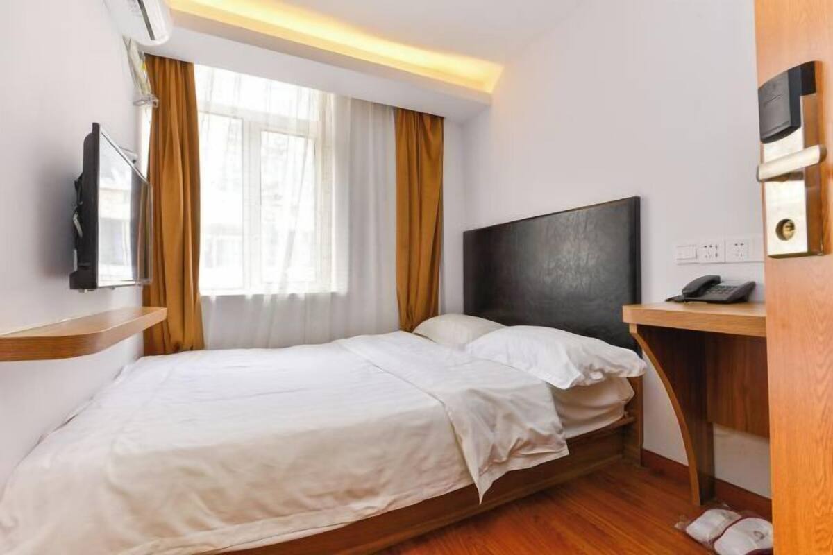 A hotel room with a bed, a desk, a phone, and a window with curtains.