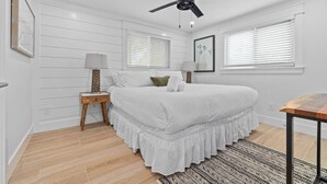 Une chambre à coucher avec un lit, des tables de chevet, un ventilateur de plafond et une fenêtre avec des stores.