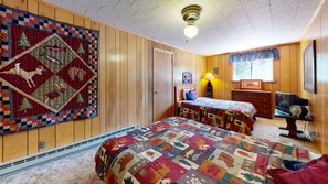 Una habitación con dos camas, una pared de madera, colcha, lámpara, cómoda y televisor.