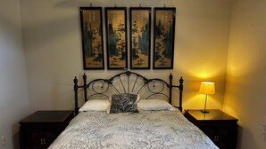 Un dormitorio con una cama, dos mesitas de noche, una lámpara y cuatro cuadros enmarcados en la pared.