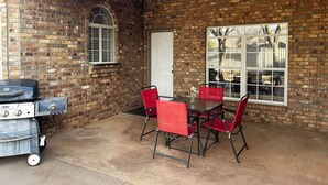Un patio cubierto con pared de ladrillo, una parrilla y sillas rojas alrededor de una mesa.