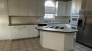 Una cocina con armarios blancos, una isla central con estufa y un refrigerador de acero inoxidable.